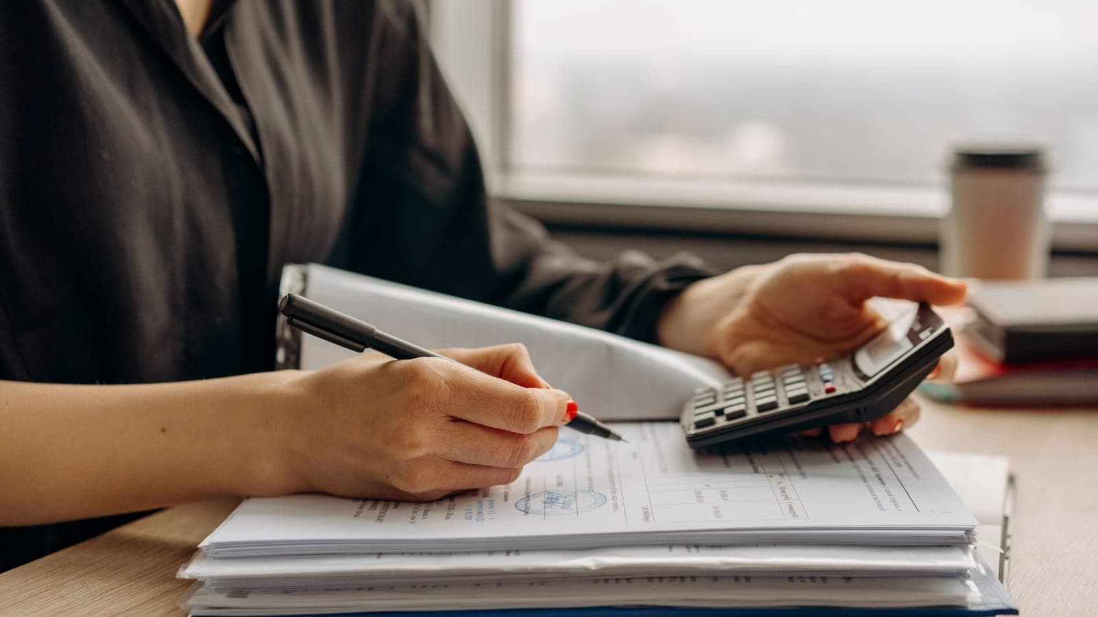 Persona fent números amb una calculadora sobre una pila de documents