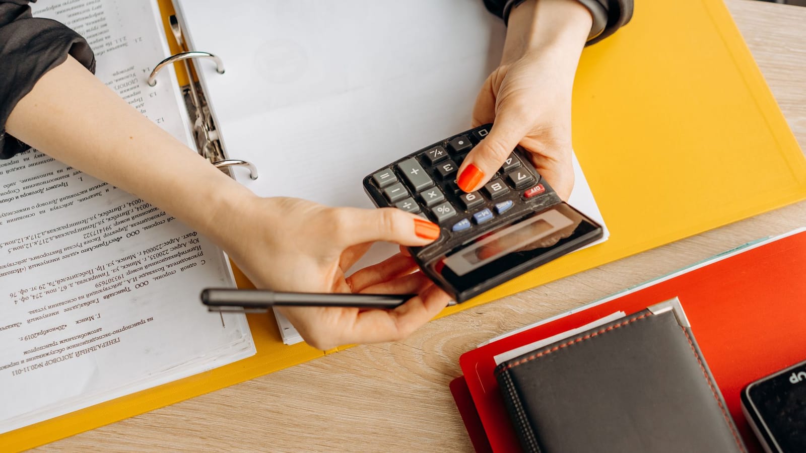 Mans fent càlculs amb una calculadora damunt d'una carpeta de documents